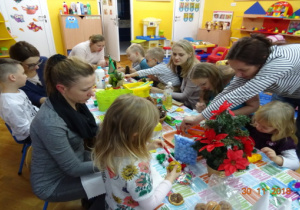 Rodzice z dziećmi tworzą dekoracje świąteczne z wykorzystaniem różnorodnych materiałów.